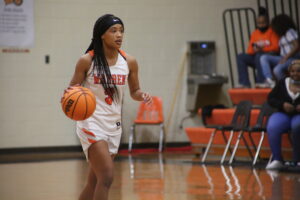 A girl in white and orange basketball uniform holding a ball.