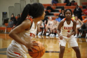Two girls playing basketball on a court with people watching.