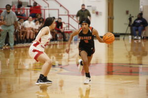 A girl dribbles the basketball while another looks on.