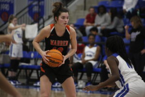 A girl holding a basketball in front of another player.