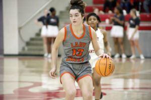 A girl in grey and orange basketball uniform holding a ball.