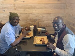 Two men sitting at a table eating food.