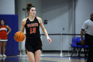 A girl in black and orange basketball uniform holding a ball.