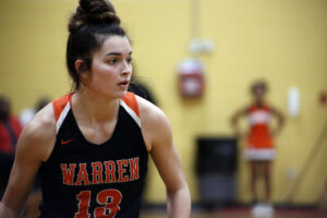 A woman in black and orange shirt holding basketball.