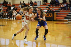 A girl in white jersey playing basketball while another girl is on the other side of her.