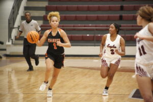 A girl in black and orange basketball uniform holding a ball.
