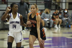 A girl in black and orange basketball uniform playing basketball.