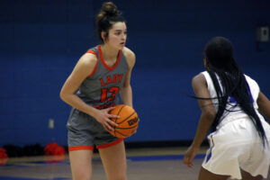 A girl in grey and orange basketball uniform holding a ball.