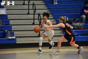 A girl dribbles the basketball while another looks on.