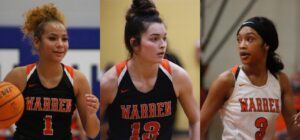 Three women are playing basketball and one is wearing a black shirt.