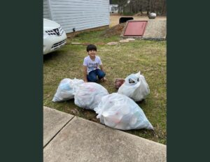 A boy sitting on the ground with some bags of trash.