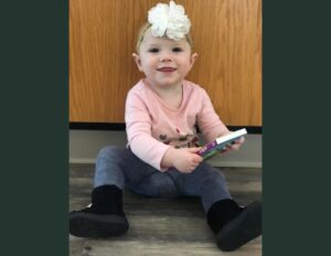 A little girl sitting on the floor holding a cell phone.