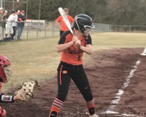 A girl in orange and black uniform holding a baseball bat.