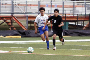 Two boys are playing soccer on a field.