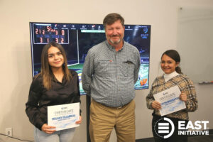 Three people holding certificates in front of a television.