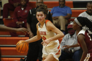 A girl dribbles the basketball in front of an audience.