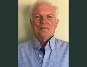 A man with white hair wearing a blue shirt and tie.