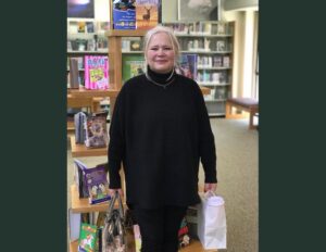 A woman standing in front of books and bags.
