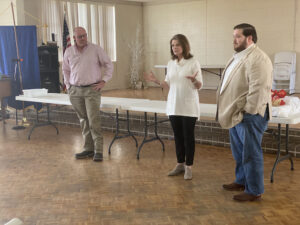 Three people standing in a room with one woman talking to another man.