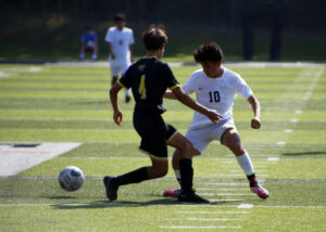 Two men playing soccer on a field with trees in the background.