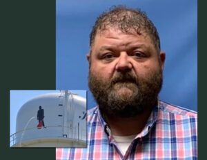 A man with a beard and plaid shirt in front of a picture.