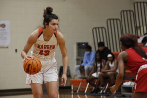 A girl in white and orange basketball uniform holding a ball.