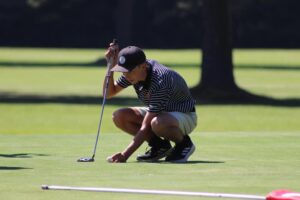 A man crouching down on the golf course holding his club.