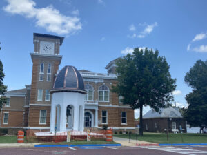 A building with a clock tower and a tree in front of it.