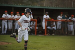 A baseball player running on the field with his bat.
