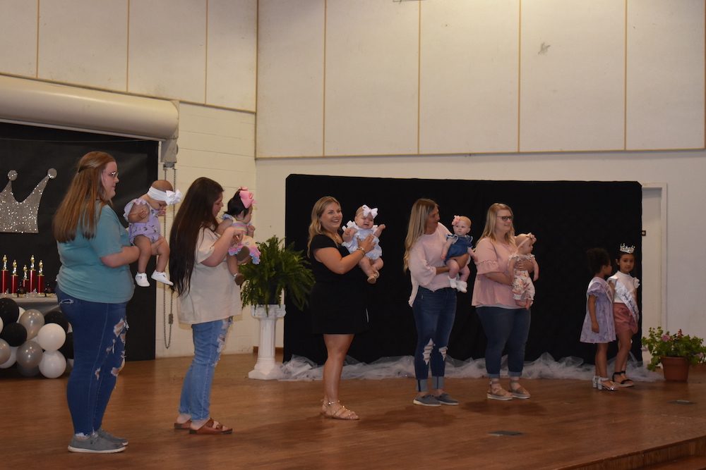 A group of people holding baby dolls on stage.