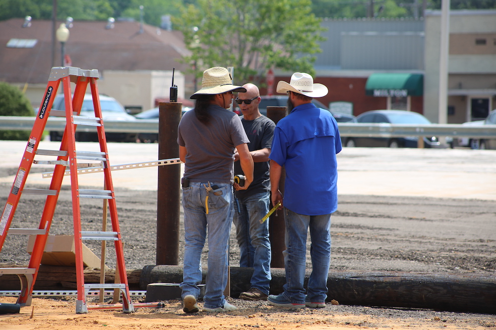 Three men standing around a fence on the side of a road.
