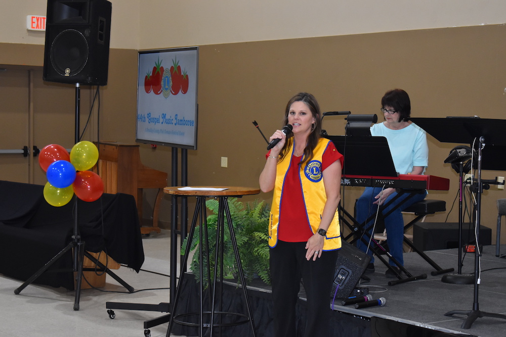 A woman standing at the microphone in front of a group.
