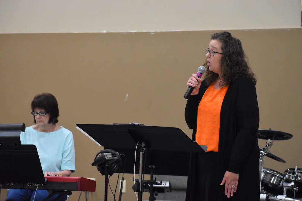 A woman is speaking into a microphone while another person watches.