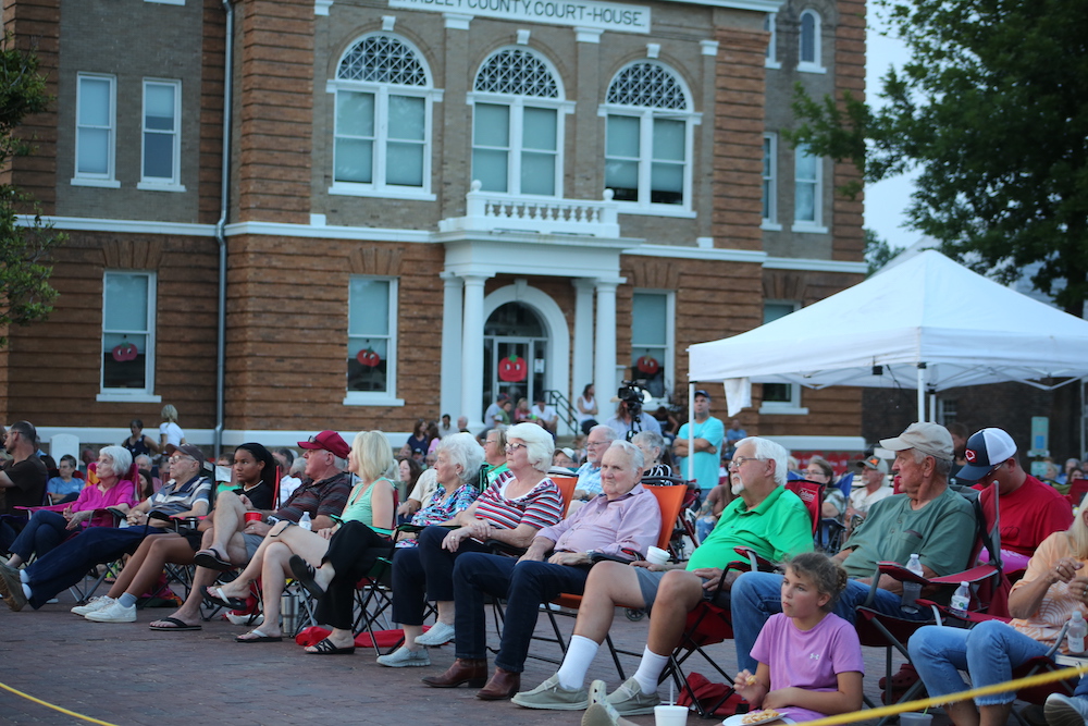 A group of people sitting in chairs on the side of a road.