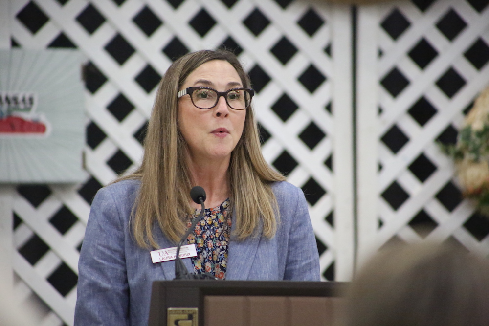 A woman in glasses is speaking at a podium.