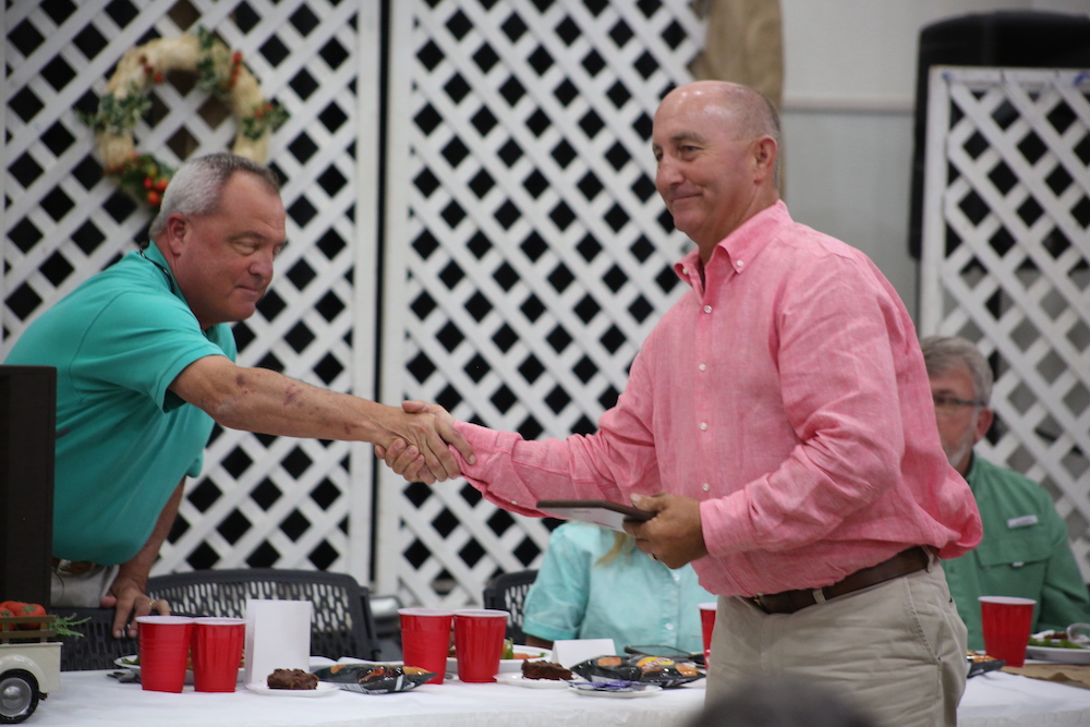 Two men shaking hands over a table with plates and cups.