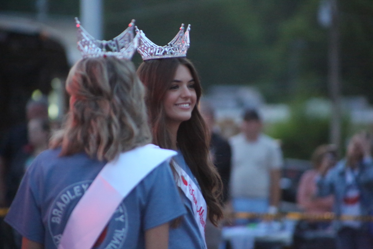 Two women in crowns are standing outside.