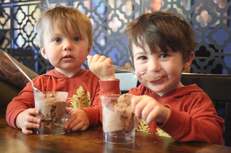 Two young boys sitting at a table with some ice cream.