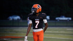 A football player in an orange uniform is walking on the field.