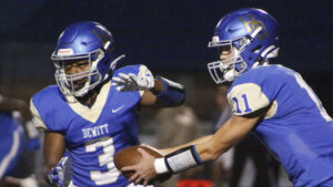 Two football players are holding hands and one is wearing a helmet.