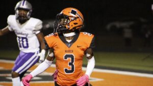 A football player in an orange uniform is walking on the field.