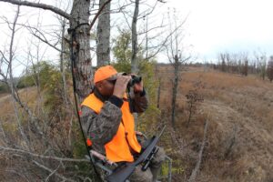 A man in an orange vest is looking through binoculars.