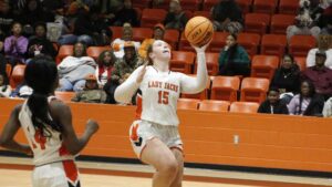A woman in white jersey holding a basketball.