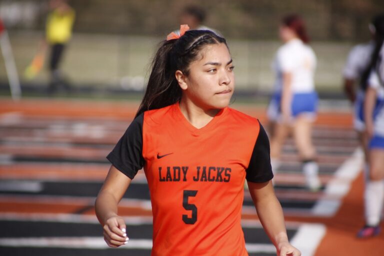 A girl in an orange and black uniform running.