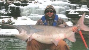 A man sitting in the snow with a large fish.
