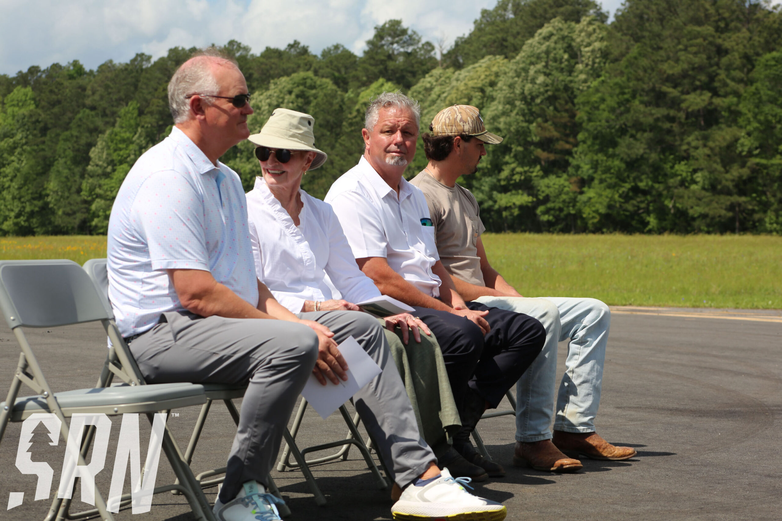 A group of people sitting on chairs in the middle of a parking lot.