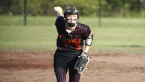 A woman in black and red baseball uniform holding a ball.