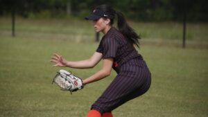 A woman in black and red baseball uniform holding a glove.